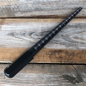 May include: A black ring sizer with white markings. The sizer is made of wood and has a black cap on one end.
