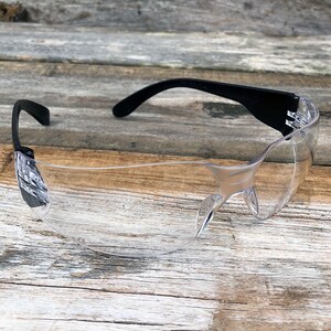 May include: Clear safety glasses with black frames. The glasses are designed to protect the eyes from debris and other hazards.