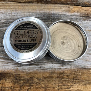 May include: A silver metal tin of GILDERS PASTE WAX in German Silver. The tin is labeled with the product name, color, and size. It covers 30 square feet or 2.78 square meters and contains 1 ounce or 30 milliliters of wax.
