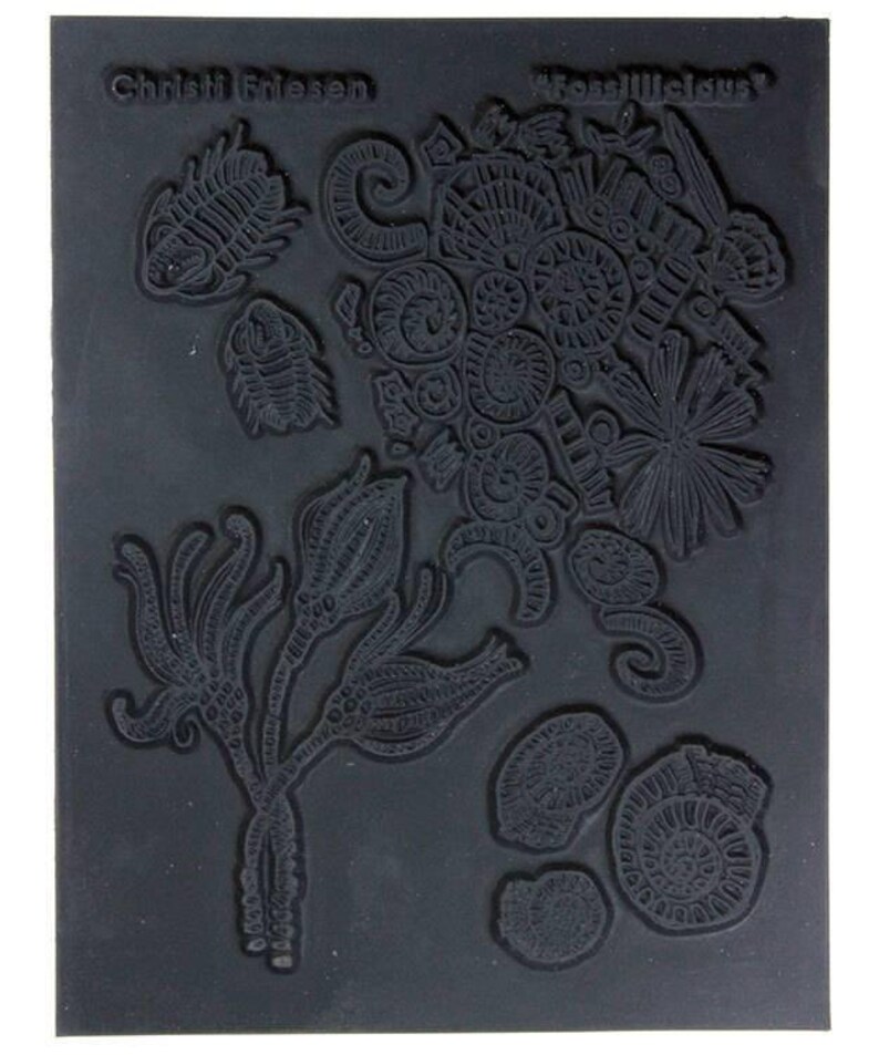 May include: Black rubber stamp with a design of various fossilized sea creatures, including trilobites, ammonites, and coral. The stamp is labeled "Fossillicious" and "Christi Friesen".
