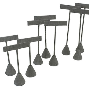 May include: Ten gray earring display stands with a textured fabric finish. Each stand has a T-shaped top with a small rectangular platform for holding earrings. The stands have a cone-shaped base.