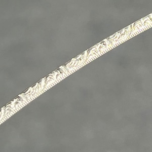 May include: Close-up of a silver wire with a decorative, embossed pattern.