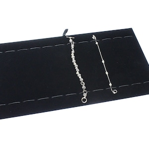 May include: Black velvet jewelry display with two silver bracelets. The display has multiple slots for holding jewelry.