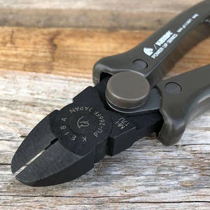 May include: Close-up of a black wire cutter with a gray handle. The cutter has the text "K.E.I.BA JAPAN PU-286FE" on the side.