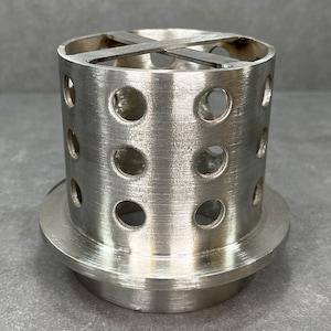 May include: A silver metal cylinder with a base and a perforated top. The cylinder has a cross-shaped design on the top.