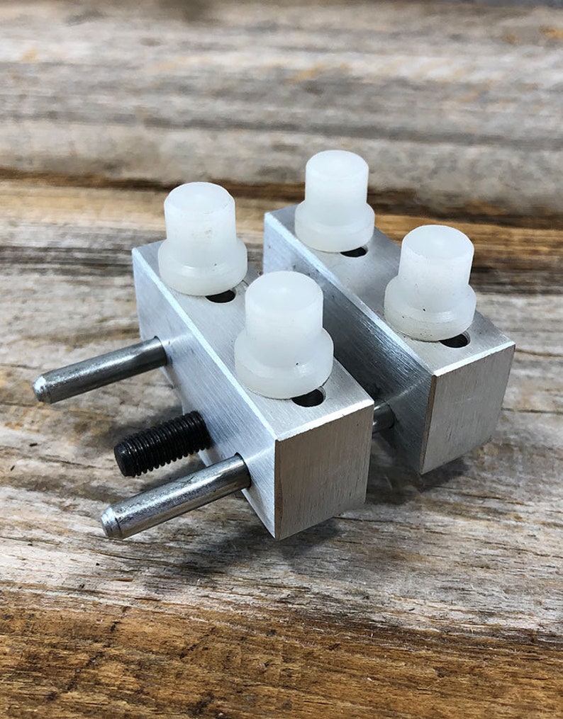 K&ouml;nnte beinhalten: Eine silberne Uhrmacher-Zwinge mit vier wei&szlig;en Kunststoff-Eins&auml;tzen. Die Zwinge hat eine Gewindestange und zwei silberne Stifte.