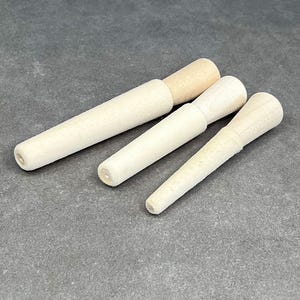 May include: Set of three wooden dowels, tapered at one end, in various sizes. The dowels are light brown and have a smooth finish.