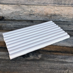 May include: A stack of white paper straws, arranged in parallel rows. The straws are cylindrical and appear to be made of paper. The background is a weathered wooden surface.