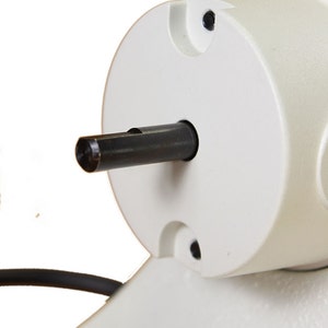 Może przedstawiać: Zbliżenie na biały silnik elektryczny z wystającym z boku czarnym wałem metalowym. Wał ma mały rowek biegnący wzdłuż jego długości.