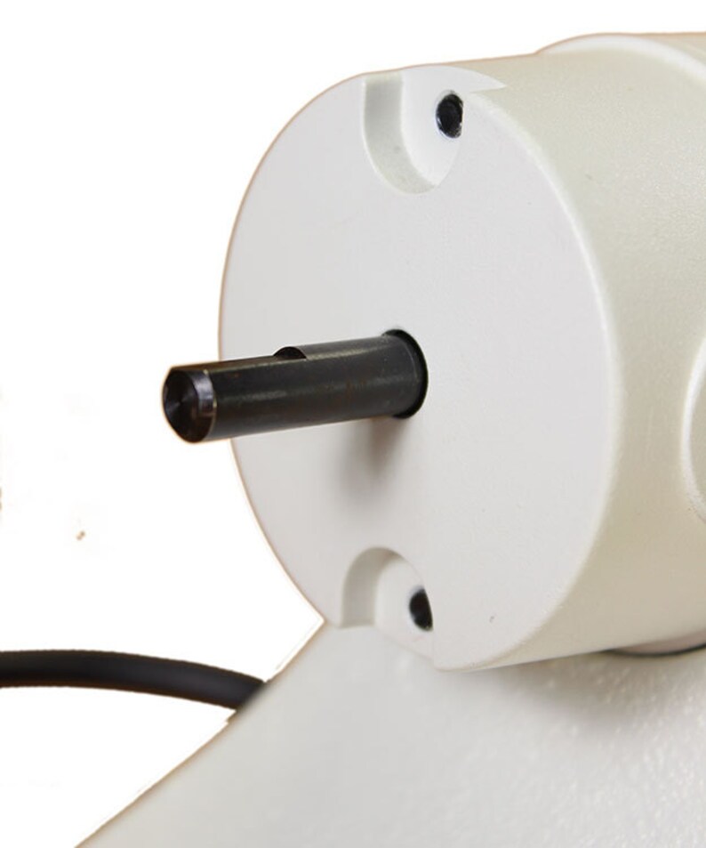 Może przedstawiać: Zbliżenie na biały silnik elektryczny z wystającym z boku czarnym wałem metalowym. Wał ma mały rowek biegnący wzdłuż jego długości.