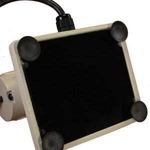 Może przedstawiać: Biała podstawa z czarną powierzchnią i czterema gumowymi stopkami na spodzie. Podstawa ma przymocowany kabel.