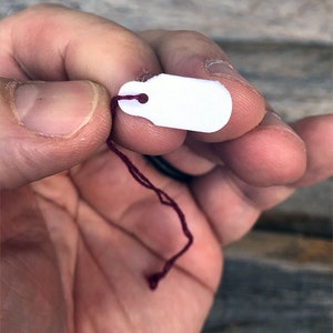 May include: A white tag with a hole in the top, attached to a maroon string.