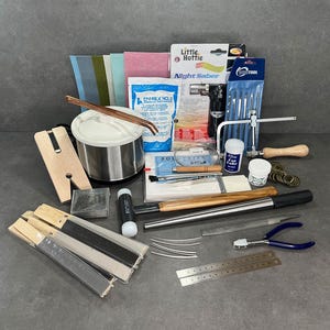 May include: A jewelry making kit with a variety of tools and supplies, including a torch, a soldering iron, a metal pot, a hammer, a saw, a ruler, and a variety of files and pliers.