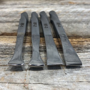 May include: Four silver metal tools with rounded ends, labeled "RC-1", "RC-2", "RC-3", and "RC-4", arranged in a row on a wooden surface.