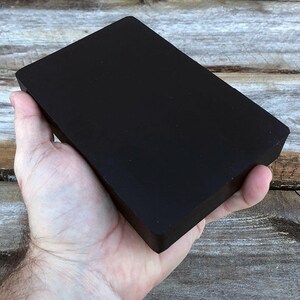 May include: A black rectangular block of wood, held in a person's hand.