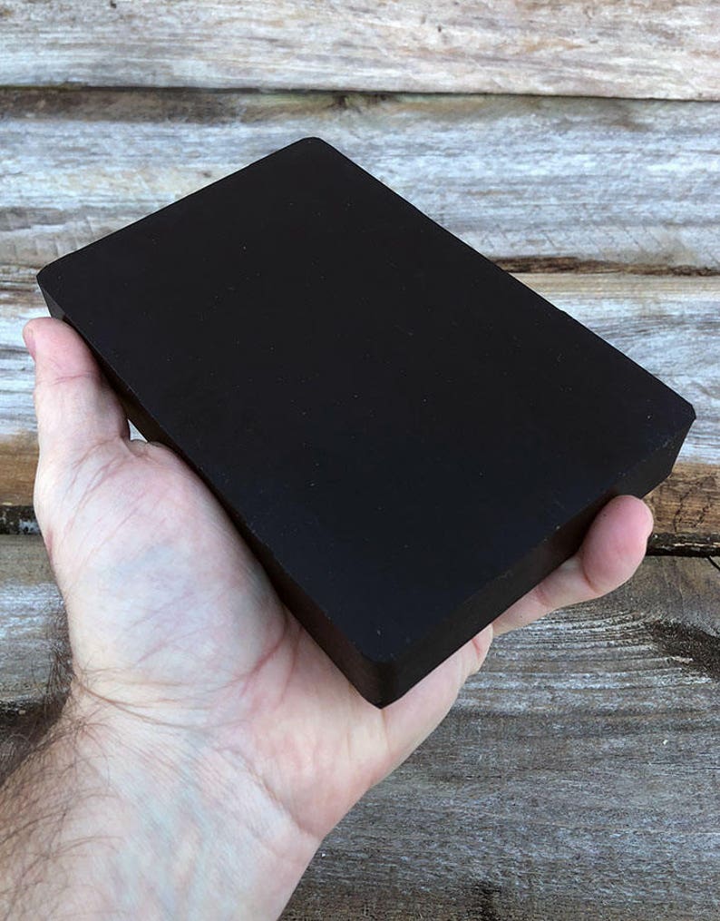 May include: A black rectangular block of wood, held in a person's hand.