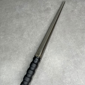May include: A silver metal ring mandrel with a black rubber handle. The mandrel is long and thin, and the handle is textured.
