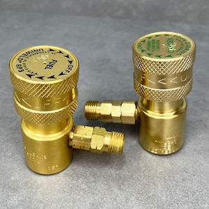 May include: Two gold-colored metal welding torch regulators with black lettering. The regulator on the left is labeled "FUEL" and the regulator on the right is labeled "OXYGEN".