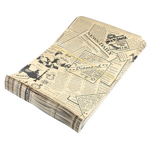 Pu&ograve; includere: Una pila di tovaglioli di carta con un design vintage di giornale. I tovaglioli sono beige con testo e illustrazioni nere, tenuti insieme da un elastico giallo. Il testo include "NEWS DAILY" e "Back To School Specials".