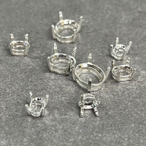 May include: Assortment of silver-toned metal settings for oval-shaped gemstones. The settings are of varying sizes and feature a prong setting.