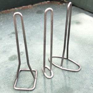 May include: Three silver metal wire stands of different sizes. The stands are shaped like a rectangle with a curved top.