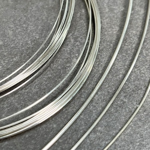 May include: A close-up of a pile of silver wire, arranged in a circular pattern. The wire is shiny and smooth, and the light reflects off of it.