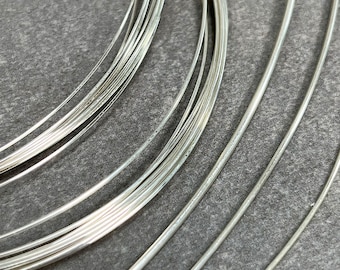 May include: A close-up of a pile of silver wire, arranged in a circular pattern. The wire is shiny and smooth, and the light reflects off of it.