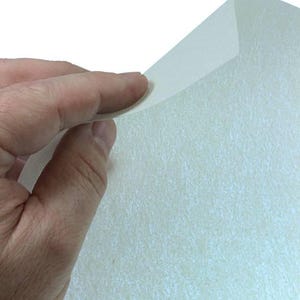 May include: A sheet of white glitter paper with a subtle iridescent sheen. The paper is textured and has a slightly rough surface.