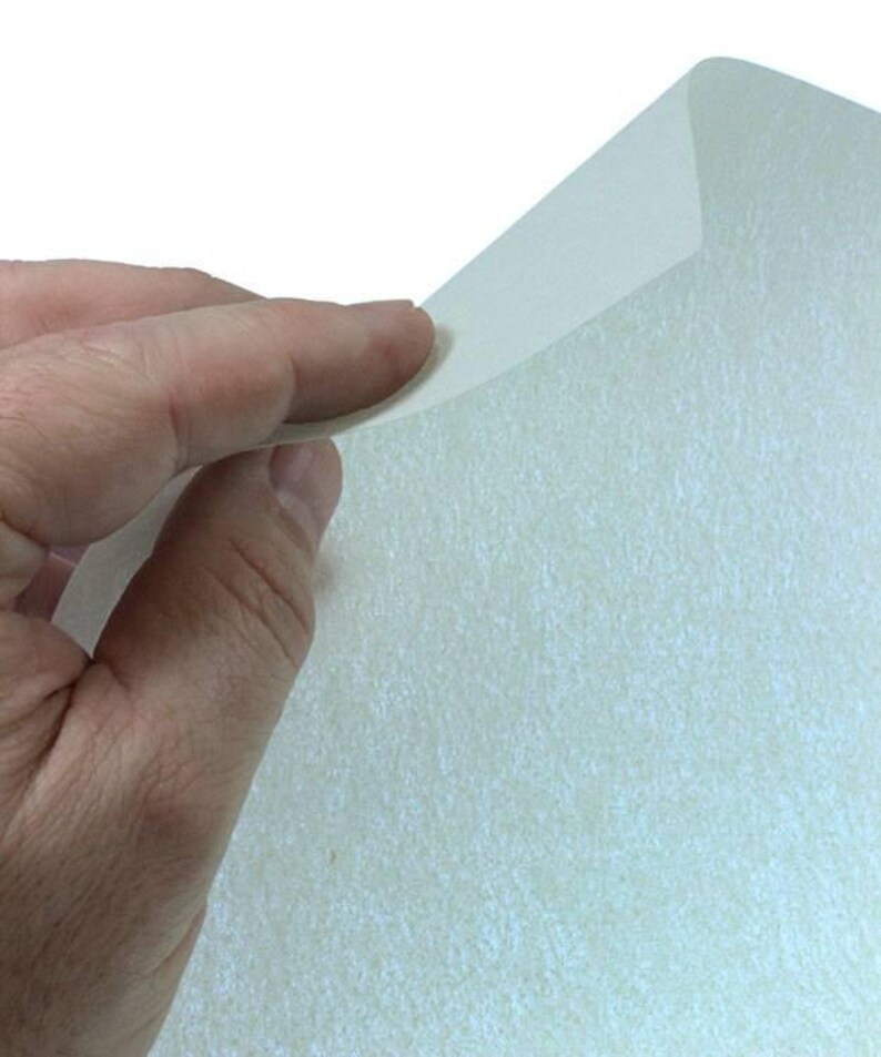 May include: A sheet of white glitter paper with a subtle iridescent sheen. The paper is textured and has a slightly rough surface.