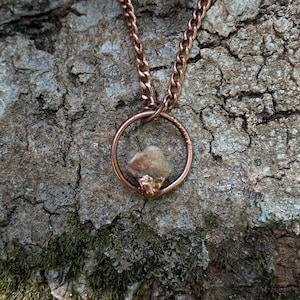 May include: A copper necklace with a small, irregular-shaped stone held within a circular pendant.