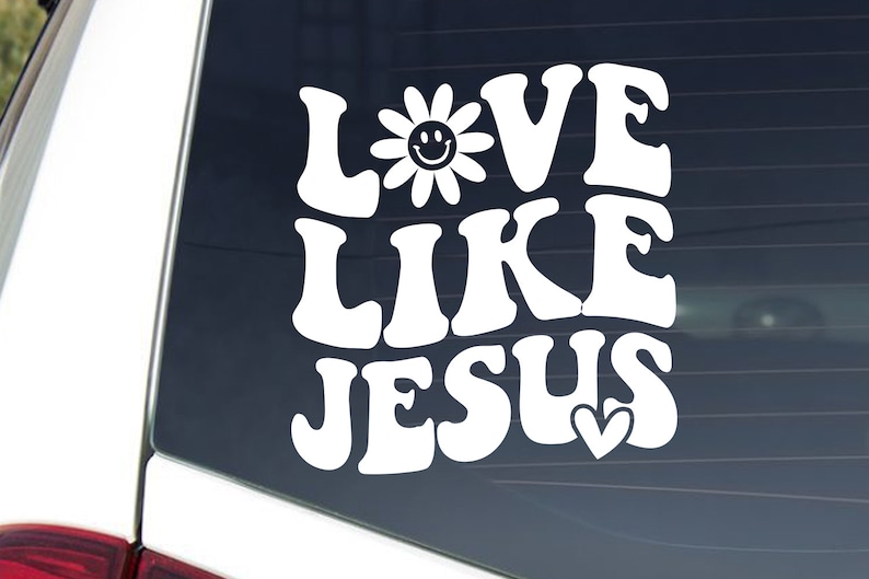 May include: White vinyl decal with the words "LOVE LIKE JESUS" in a retro font. A smiling daisy replaces the letter "O" in "LOVE", and a heart replaces the "S" in "JESUS".