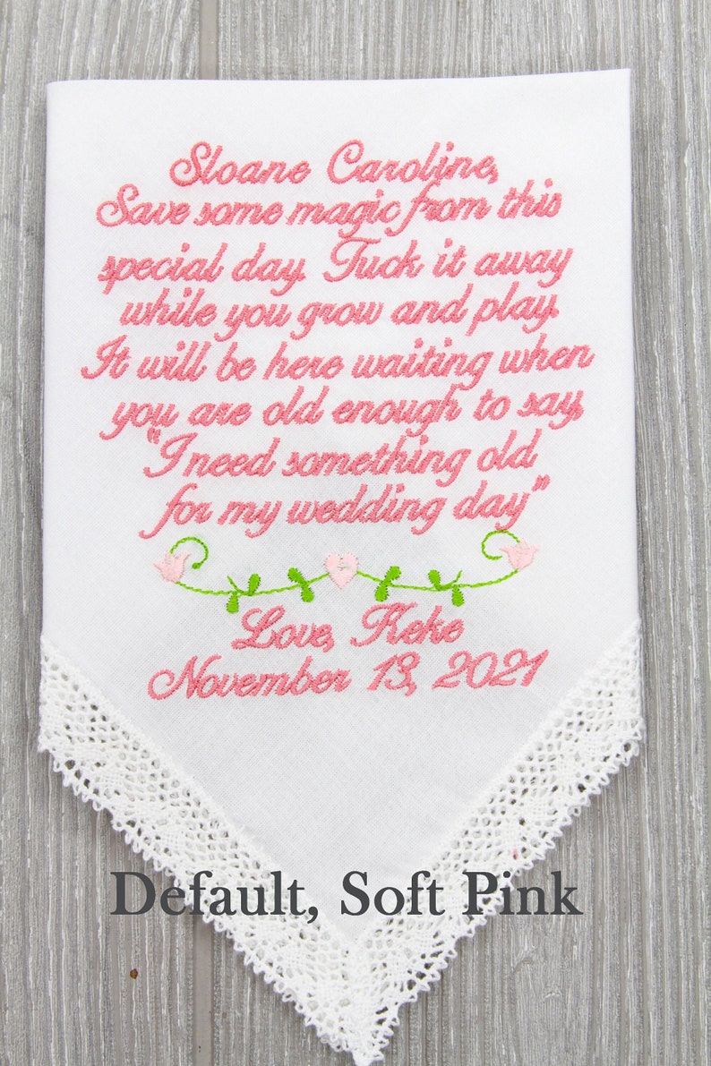 Puede incluir: Un pa&ntilde;uelo blanco con texto bordado en rosa que dice "Sloane Caroline, Save some magic from this special day. Tuck it away while you grow and play. It will be here waiting when you are old enough to say "I need something old for my wedding day." Love Keke November 13, 2021". El pa&ntilde;uelo tiene un borde de encaje blanco y est&aacute; etiquetado como "Default, Soft Pink".