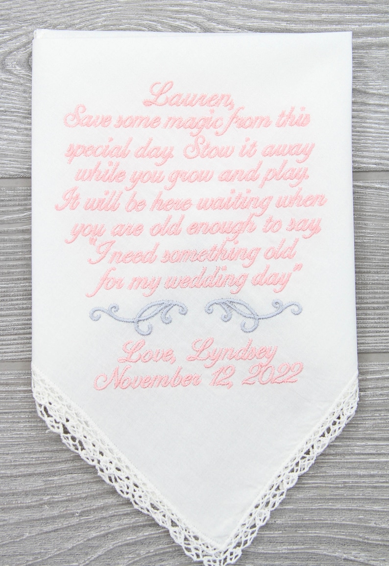 Puede incluir: Un pa&ntilde;uelo blanco con borde de encaje y texto bordado en rosa que dice "Lauren, Guarda algo de magia de este d&iacute;a especial. Gu&aacute;rdalo mientras creces y juegas. Estar&aacute; aqu&iacute; esper&aacute;ndote cuando seas lo suficientemente mayor para decir "Necesito algo viejo para mi d&iacute;a de boda." Con amor, Lyndsey 12 de noviembre de 2022"
