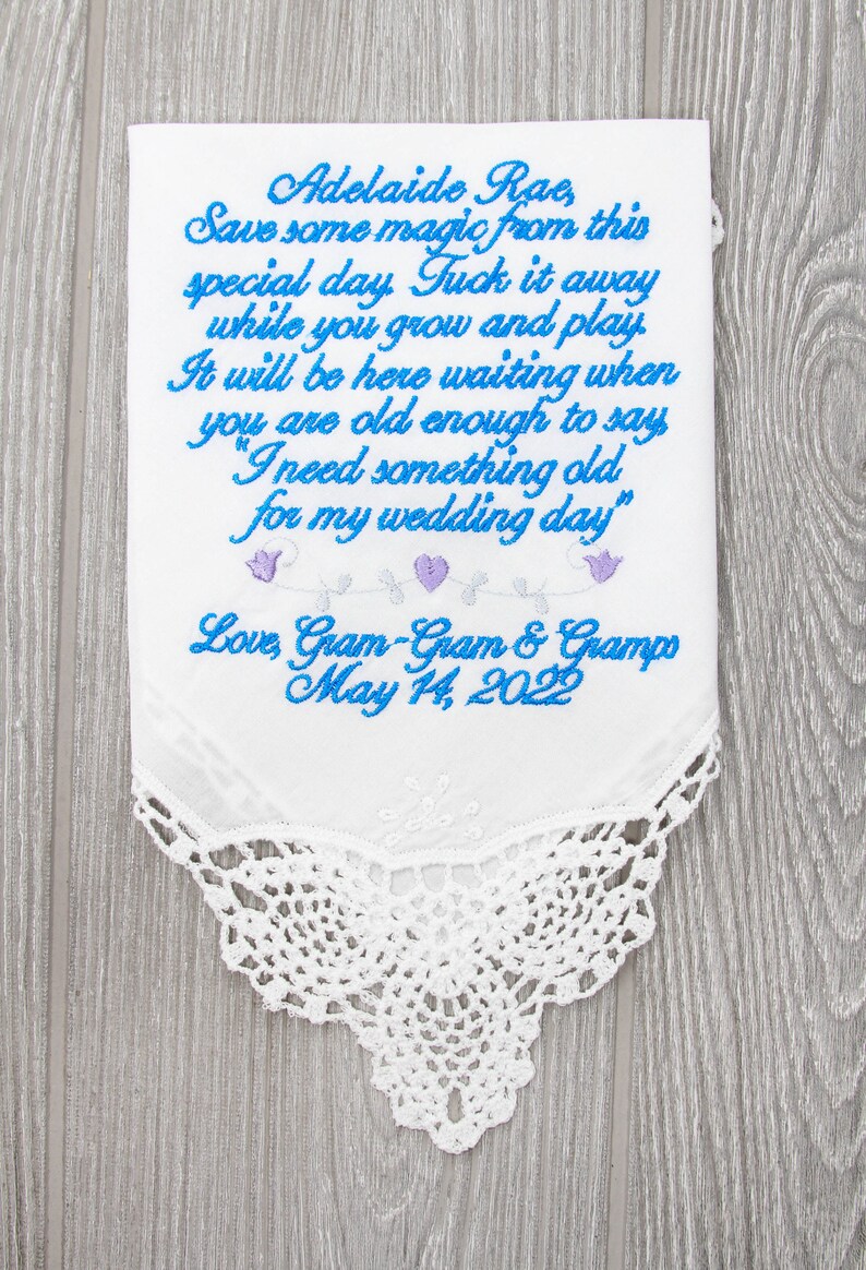 Puede incluir: Un pa&ntilde;uelo blanco bordado con bordados azules y morados. El texto dice "Adelaide Rae Save some magic from this special day. Tuck it away while you grow and play. It will be here waiting when you are old enough to say "I need something old for my wedding day" Love, Gram-Gram & Grampo May 14, 2022"