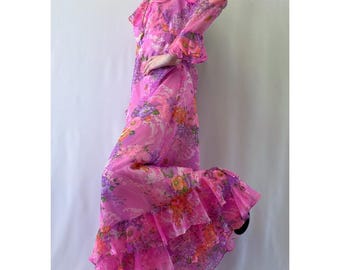 Vestido largo de manga larga en rosa brillante de los años 60 o 70 con estampado floral en tonos morado, naranja, verde y blanco y detalles de volantes.