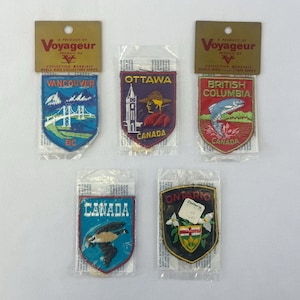 May include: Five embroidered souvenir patches from the Voyageur World Wide Collectors Series. The patches feature designs for Vancouver, Ottawa, British Columbia, Canada, and Ontario, each sealed in individual clear plastic packaging.