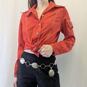 May include: A red button-up shirt with white stitching and a silver chain belt with oval-shaped charms.