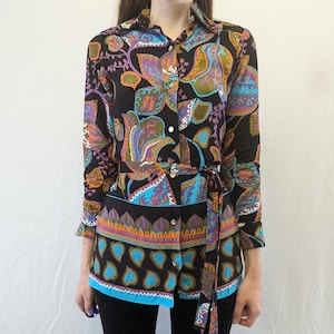 May include: A long-sleeved shirt with a paisley print in shades of blue, orange, purple, and green. The shirt has a button-up front and a tie belt at the waist.