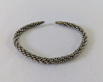 May include: A silver braided bangle bracelet with a simple design.