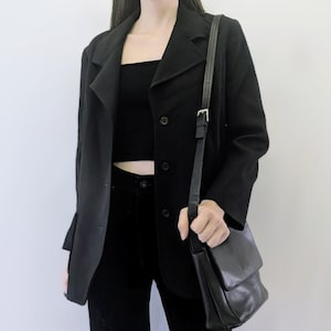 May include: A black blazer with a single-breasted closure and a black leather shoulder bag. The blazer has a lapel collar and two front pockets.