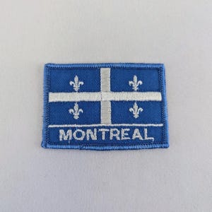 May include: A blue and white embroidered patch with the text "MONTREAL" and a stylised white cross with four fleur-de-lis on a blue background.