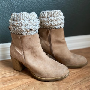 May include: A pair of brown suede ankle boots with a chunky heel. The boots have a white and beige knitted cuff around the top.