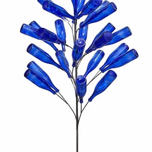 May include: A bottle tree sculpture featuring numerous cobalt blue glass bottles attached to a central dark metal rod. The bottles are arranged in a branching pattern, extending outward from the main stem to create a tree-like structure.