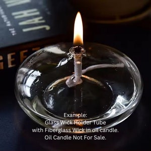 May include: A clear glass wick holder tube with a fiberglass wick and a lit flame. The text "Example: Glass Wick Holder Tube with Fiberglass Wick in oil candle. Oil Candle Not For Sale." is visible below the wick holder.