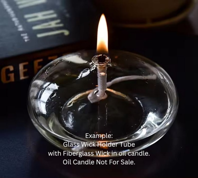 May include: A clear glass wick holder tube with a fiberglass wick and a lit flame. The text "Example: Glass Wick Holder Tube with Fiberglass Wick in oil candle. Oil Candle Not For Sale." is visible below the wick holder.