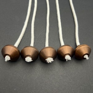 May include: Five brown metal candle wick holders with white cotton wicks. The wicks are threaded through the holders and hang down.