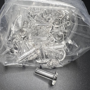 May include: A clear plastic bag filled with numerous clear glass and silver metal bottle stoppers. One stopper is outside the bag, showing a silver metal body and a clear glass top. The stoppers have a decorative design.