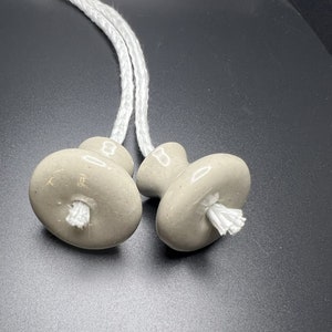 May include: Two gray ceramic pull cords with white rope. The cords are tied together and the ceramic ends are shaped like a mushroom.