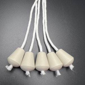 May include: Five white cotton lamp wicks with beige ceramic bases. The wicks are tied together at the top.
