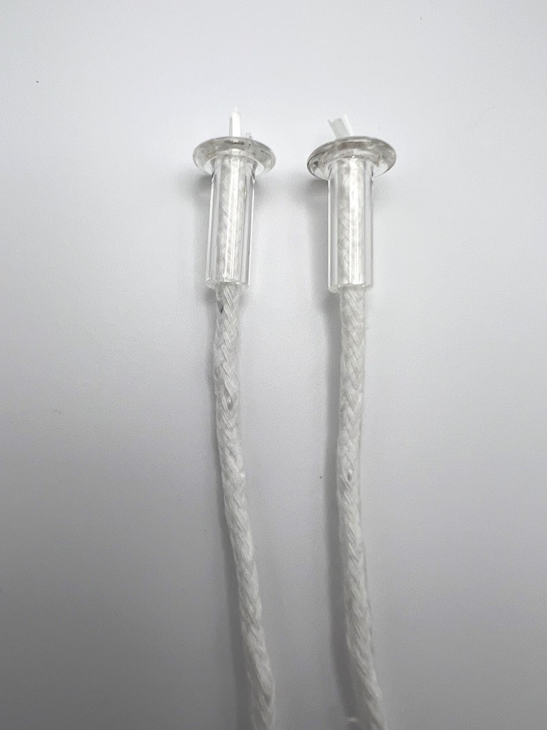 May include: Two white cotton wicks with clear plastic tops. The wicks are braided and have a small loop at the top.